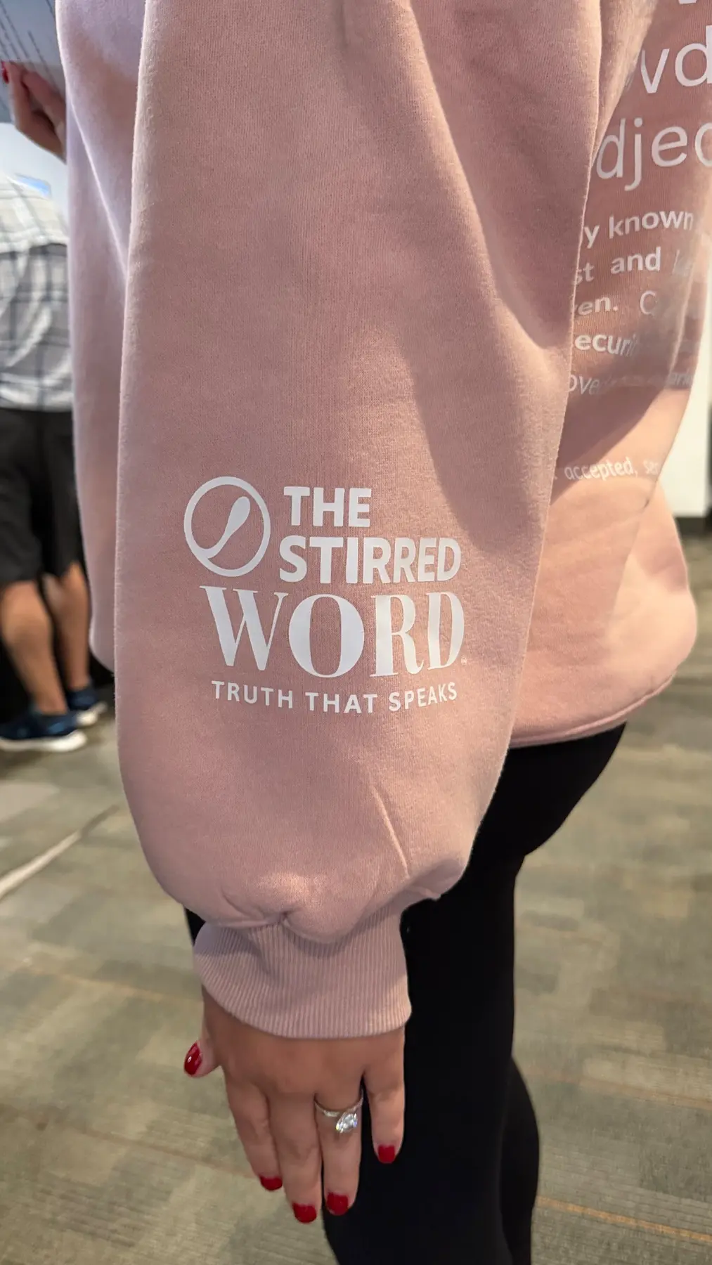 The Stirred Word logo printed on a blush sweatshirt sleeve